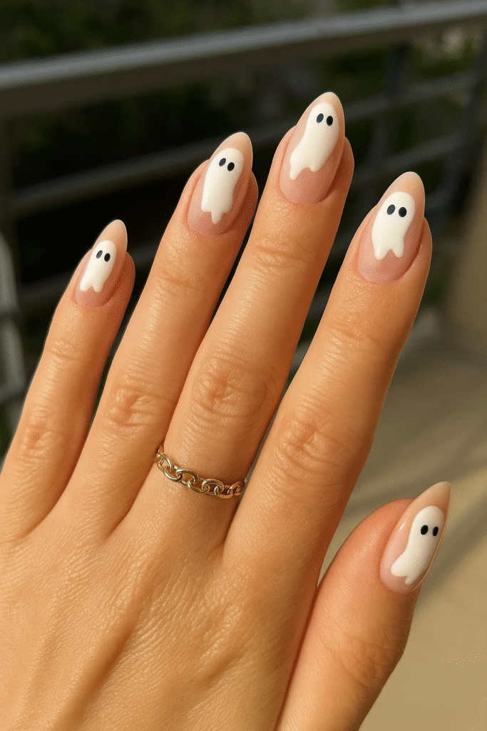 Ghost Halloween nails with a nude base, featuring playful ghost shapes and tiny black eyes for a cute spooky look.