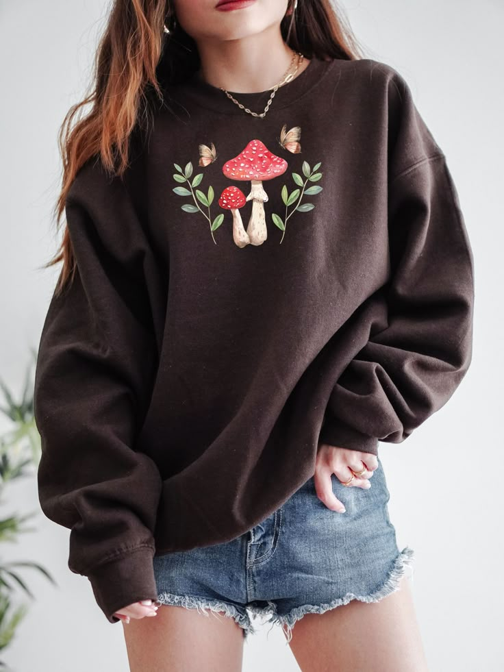Oversized chocolate sweatshirt with mushroom graphic styled casually with denim shorts—easy, comfy look that doubles as sweatshirt-dress vibes.