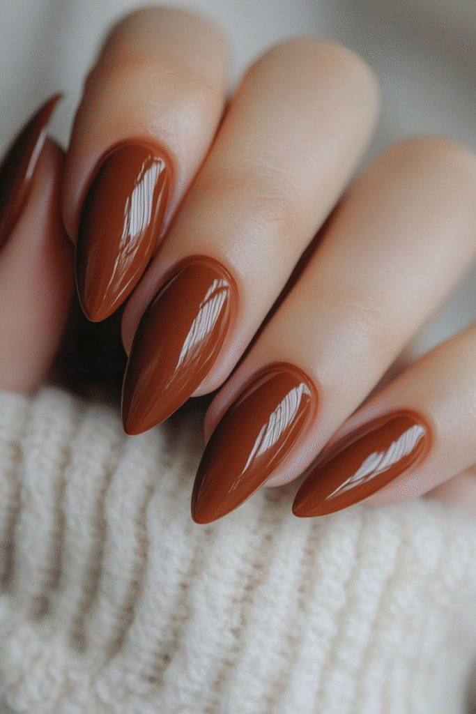 Deep toffee brown almond nails with high-shine gel look on a cozy sweater.