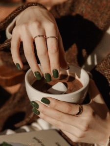 Matte forest green square nails holding a mug, accented with small gold charms.