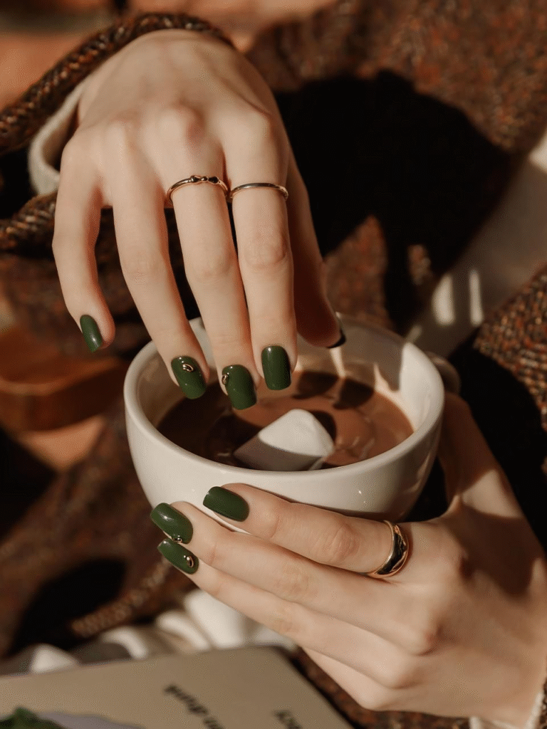 Matte forest green square nails holding a mug, accented with small gold charms.