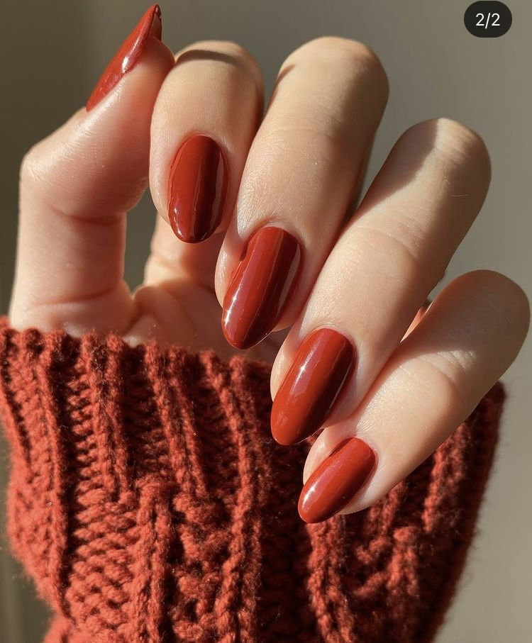 Burnt brick red oval nails, shiny finish, peeking from a rust cable-knit sleeve.