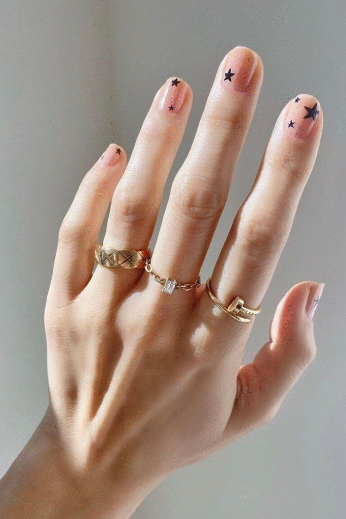 Minimal micro French nails concept with scattered tiny black star decals on a clear, natural base; delicate and airy.