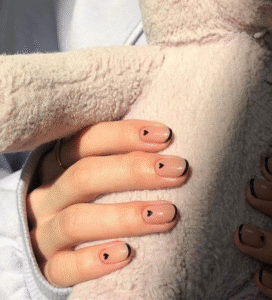 Short nude nails with black micro French outline and tiny black heart accents; glossy neutral base.