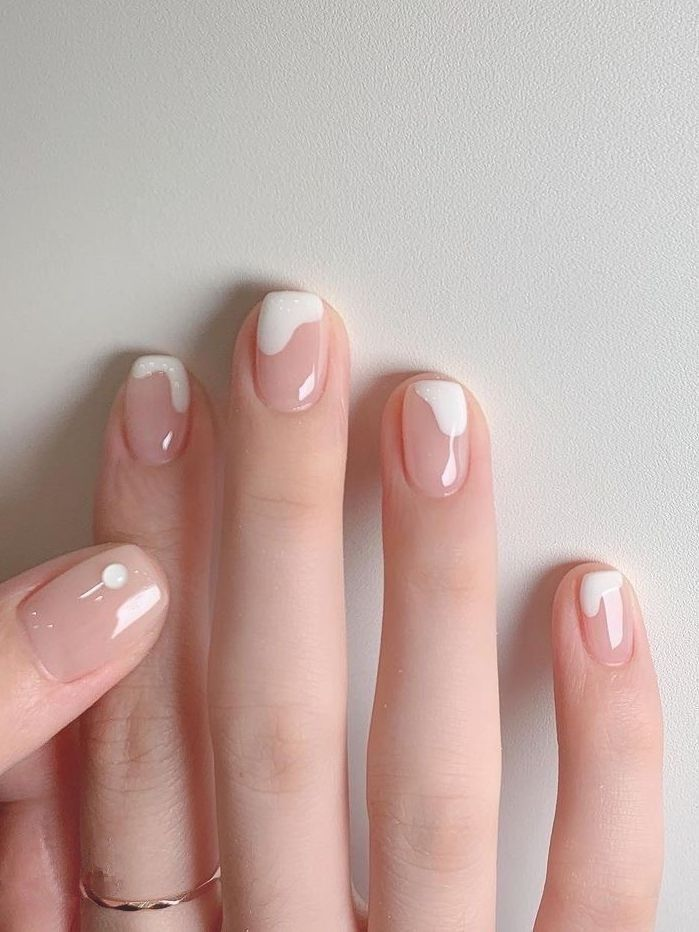 Milky pink short nails with abstract white micro French drips and a single tiny white dot accent—clean, modern design.
