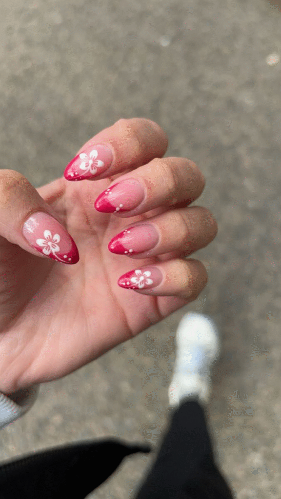 Almond nails with glossy cherry-red French tips, white hibiscus flowers and micro dot trails over a nude jelly base.
