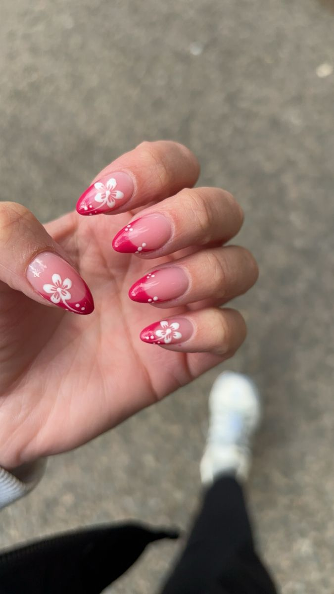 Almond nails with glossy cherry-red French tips, white hibiscus flowers and micro dot trails over a nude jelly base.