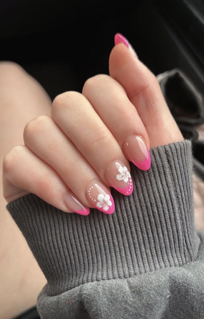 Almond nails featuring neon-pink French tips and two white hibiscus accent nails with dotted curves on a sheer base.