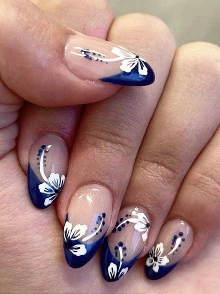 Short almond nails with deep navy French tips, white hibiscus flowers and dotted sprays on a transparent nude base.