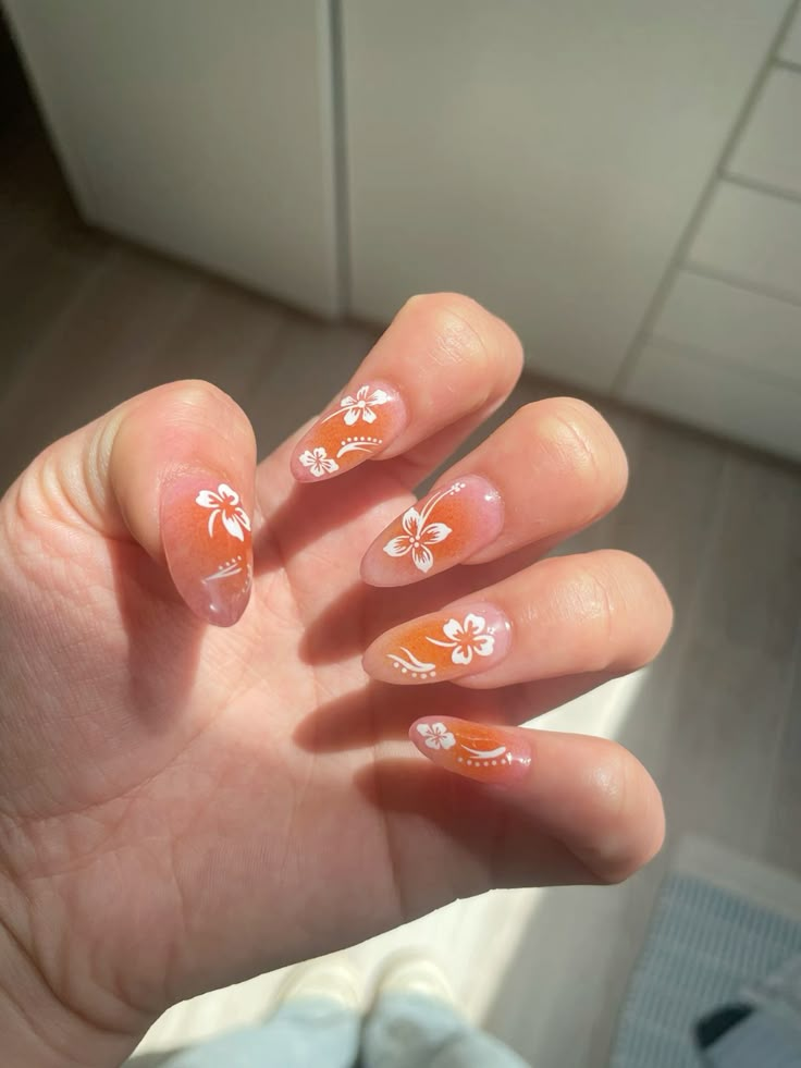 Almond nails with orange-to-pink sunset gradient tips, white hibiscus flowers and curved dotted accents.
