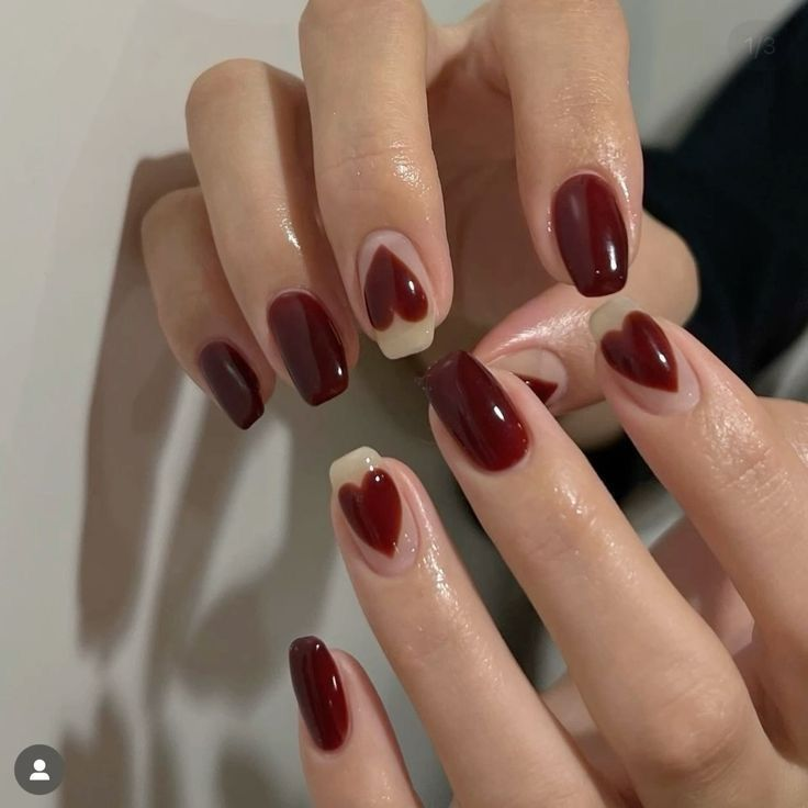 Deep cherry coded nails with negative-space heart accents on a sheer nude base, glossy almond shape.