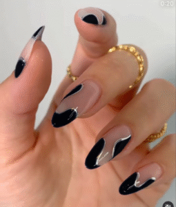 Nude base almond nails with abstract black wavy French swirls and a glossy finish; gold stacking rings.