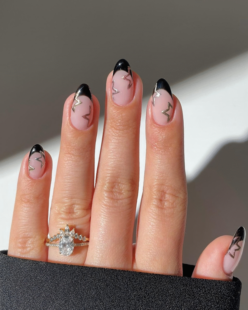 Nude almond nails with black French tips and metallic silver lightning-bolt accents; bright natural light.