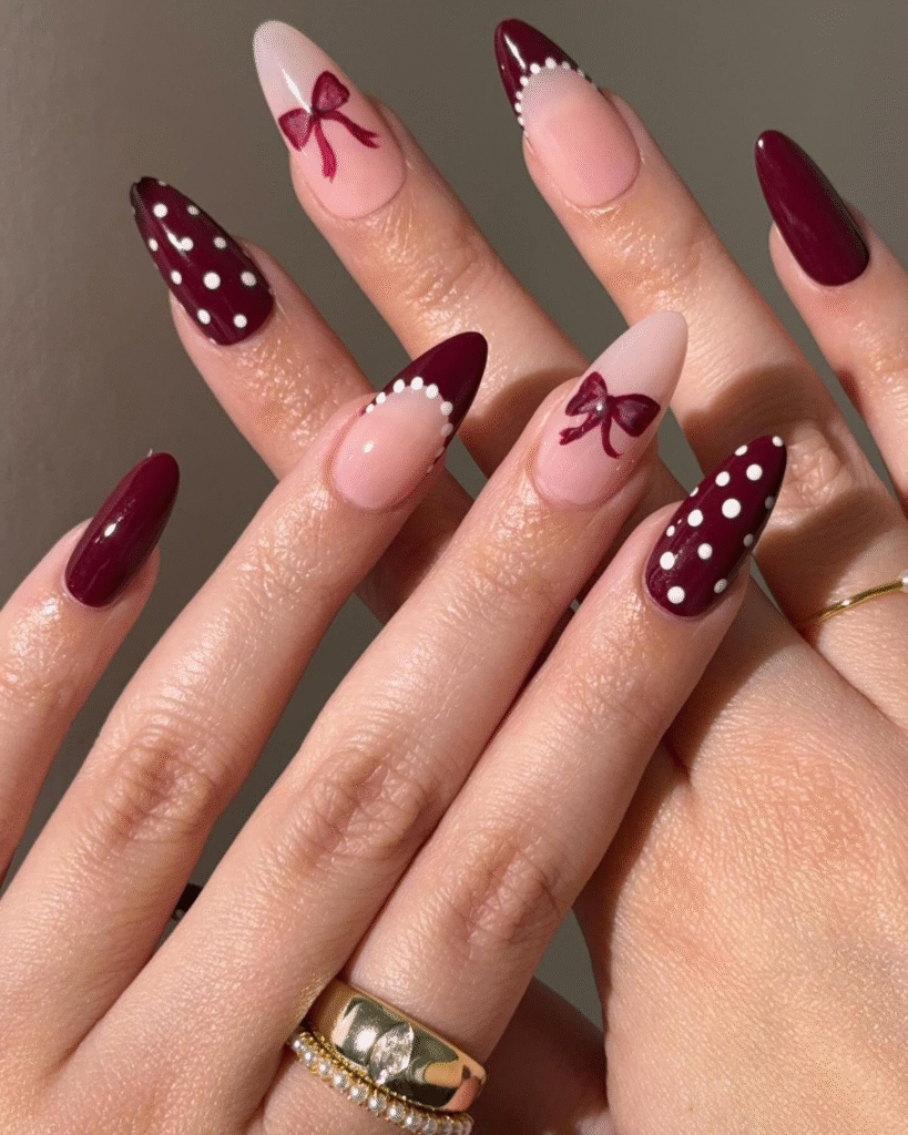 Burgundy coquette nails with dots and ribbon accents over nude base.