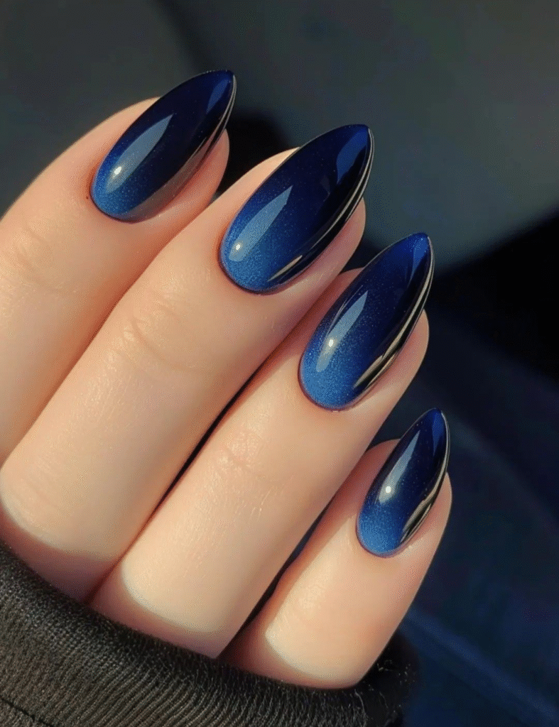 Close-up of almond-shaped nails in deep sapphire blue gel with a subtle shimmer and mirror-like shine.