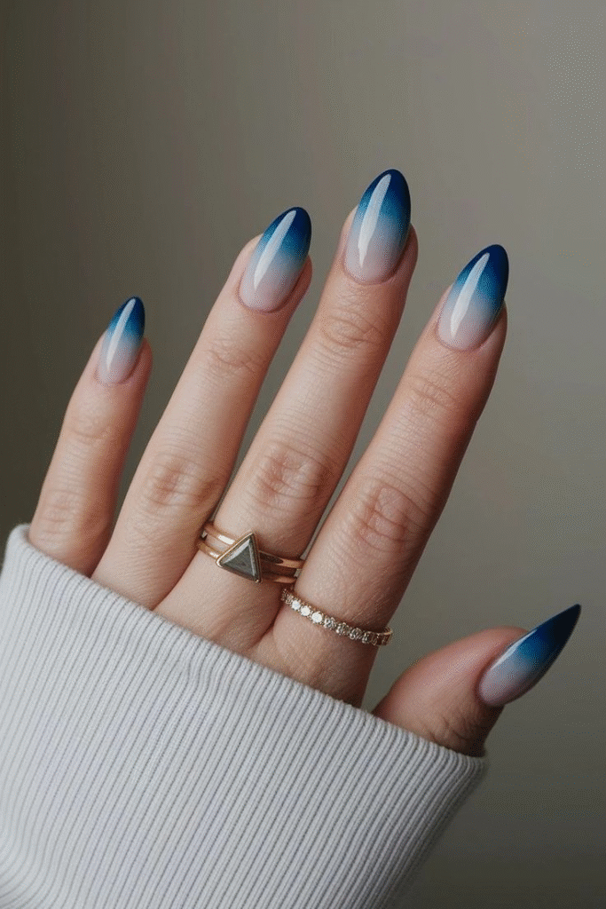 Almond nails with a sheer nude base blending into teal and royal-blue tips, high-gloss finish.