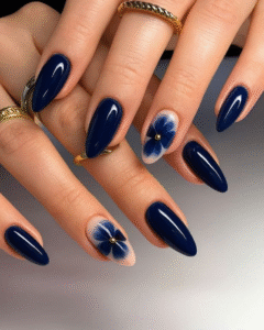 Navy almond nails with a single blurred blue flower accent on two nails; gold micro-stud centers.