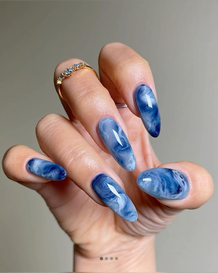 Almond nails with translucent blue jelly layers and smoky white swirls creating a water-like marble effect.