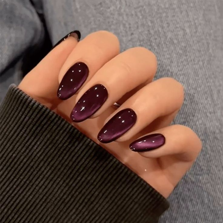 Deep plum cat-eye manicure on oval nails with a soft reflective line.