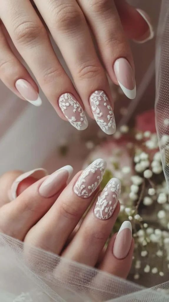Bridal French almond nails—sheer pink base with white tips and lace-like 3D floral accents; veil and baby’s-breath in background.