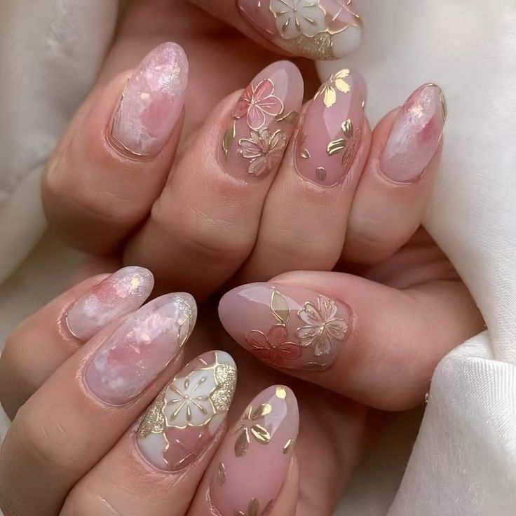 Almond blush marble bridal nails with gold leaf and floral accents; glossy finish.