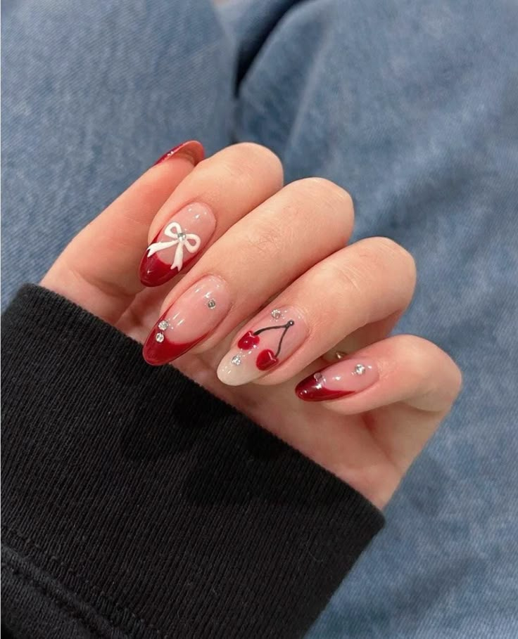 Almond aesthetic nails with white French tips and tiny red cherry accents, photographed outdoors in warm light.