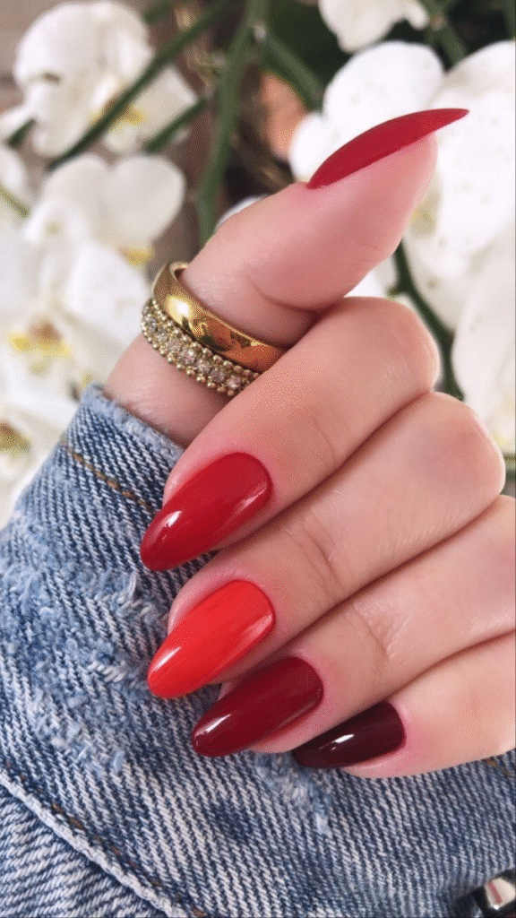 Red gradient Skittle / Mismatched palettes almond manicure close-up with gold ring.