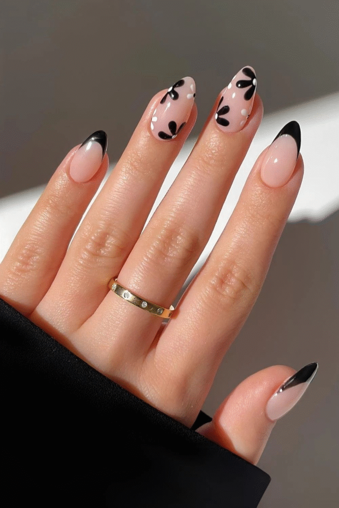 Nude almond nails with slim black French tips and bold black petal art with white dots on accent nails.